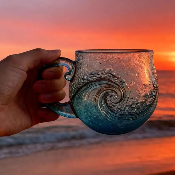Ocean Wave Glass Mug held up against a sunset over the sea